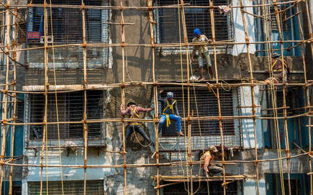 Mumbai, India - March 20, 2021 : Construction workers building a bamboo structure on a building wall to initiate the building maintenance. No protective gears.のeditorial素材