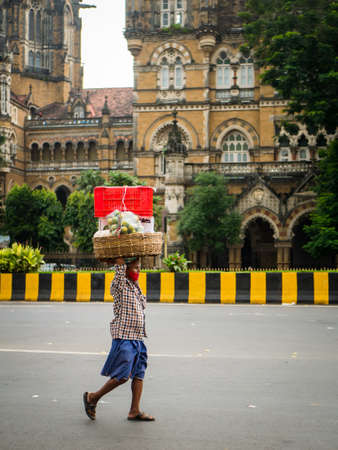 MUMBAI, INDIA - October 2, 2021 : Unidentified porter wearing covid-19 mask carrying fruits cart at CST station, Mumbaiのeditorial素材