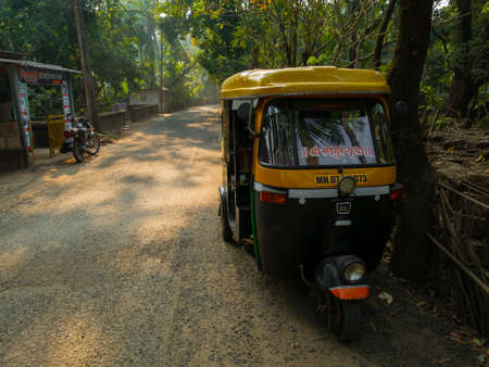 Malvan, INDIA - December 19, 2021 : Auto rickshaw standing on a road in a Picturesque lane of a small Indian village in Konkan surrounded by coconut trees.のeditorial素材