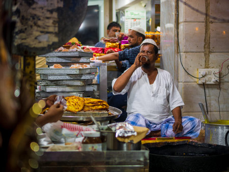 Mumbai, India - May 1, 2022 : Muslim male vendor cooking selling halal foods and drinking tea at...
