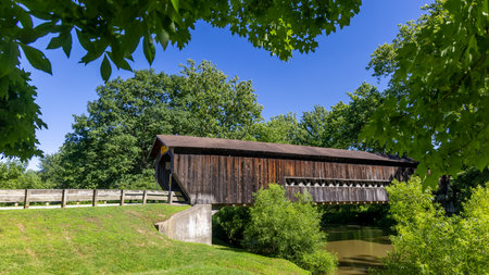 Old wooden covered bridge over the river with green trees and blue skyの写真素材