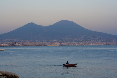Mt.Vesuvius view from Naples at dusk. A boat chugs along the Bay of Naples