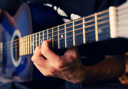 The person plays a guitar, fingers hold a chord