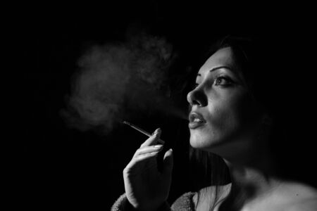 Portrait of the woman with a cigarette and a smoke against a dark background
の写真素材