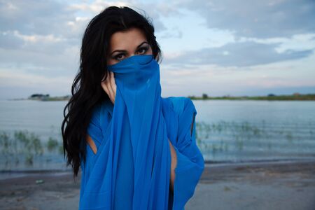 The girl covers the person with a dark blue material, against lakeの写真素材