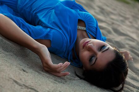 The beautiful girl in a dark blue dress has a rest on a beachの写真素材