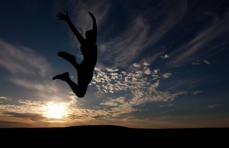 The silhouette of the guy against a decline, the beautiful sky, jumps upwardsの写真素材
