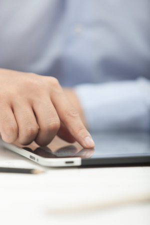 Hands of the man in the blue shirt are holding a tablet computer
