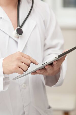Doctor working with a tablet computer, a stethoscope hanging around his neckの写真素材