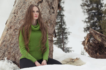 Girl in green in the mountains in winter, standing, sitting at stumpの写真素材