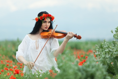 A girl with a violin in a white shirt on a poppy fieldの写真素材