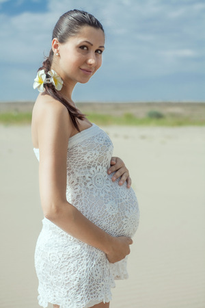 Pregnant woman in white bikini posing on the beachの写真素材