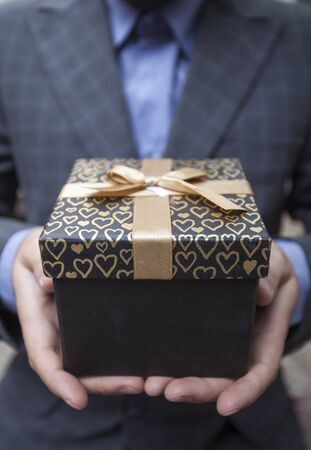 Man's hands keep a box in a business suit wrapped up by a bowの写真素材