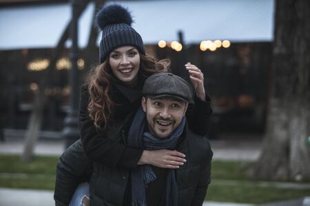 Young couple having fun outdoors at winter fair. Wearing warm clothes, hats and scarfs. Visiting christmas market in Vienna, Austria. Everything is decorated with festive string lights. Evening or night with beautiful lights lightning the scenes.の写真素材
