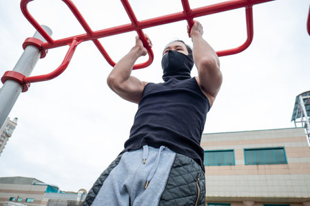 The guy is pushing up on the bars, in a black T-shirt and mask, in quarantine