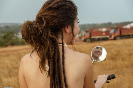 A woman sits on a motorcycle in a field waiting for sunset, back viewの写真素材