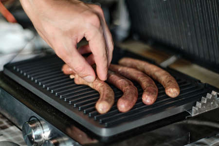 Man's hand lays out raw sausages on the grill, close up shotの写真素材