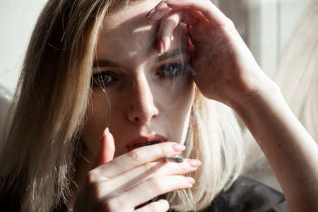 Close-Up Of Young Woman Smoking Cigarette By Windowの写真素材