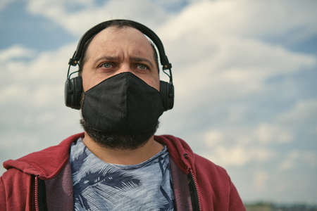 Middle-aged European man in headphones outdoors listening to music against the background of the skyの写真素材