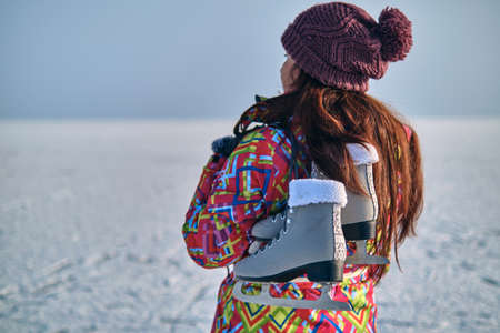 A woman in a ski suit holds skates on her shoulder and looks into the distance, after skiing on a frozen lakeの写真素材