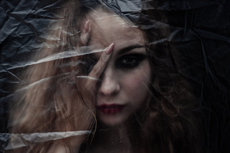 Young beauty sad woman trapped behind a plastic sheet as protection against COVID-19. Nicely fits for book coverの写真素材