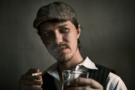 Young guy smoke a cigarette and drinks whiskey, blows smoke, dressed in a retro style, in a beret, cinematic shot, big closeupの写真素材