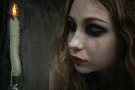 Beautiful sad young girl looking out the window with a candle, good for book coverの写真素材