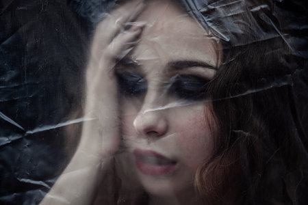 Young beauty sad woman trapped behind a plastic sheet as protection against COVID-19. Nicely fits for book coverの写真素材