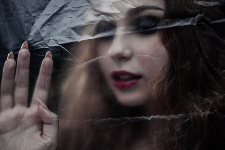 Young beauty sad woman trapped behind a plastic sheet as protection against COVID-19. Nicely fits for book coverの写真素材
