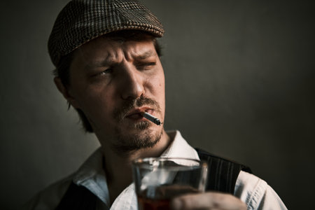 Young guy smoke a cigarette and drinks whiskey, blows smoke, dressed in a retro style, in a beret, cinematic shot, big closeupの写真素材