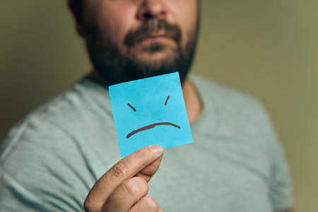 A bearded European man holds a orange sticker in front of him, with a sad smileyの写真素材
