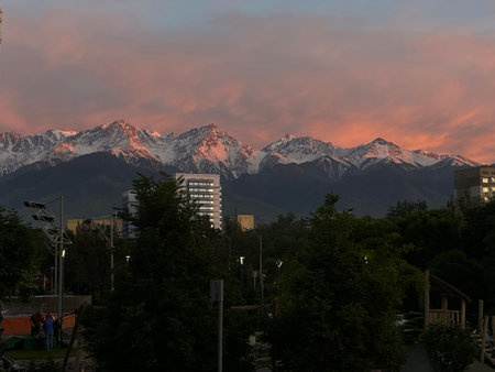 Cityscape view featuring snow-capped mountains during a vibrant sunset. An urban environment blends with natural beauty creating a serene and picturesque scene.の写真素材