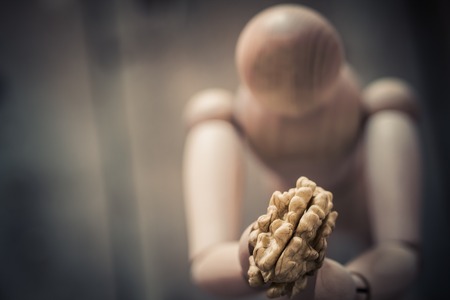 Wooden figure holding a peeled walnuts on an old wooden table.の写真素材