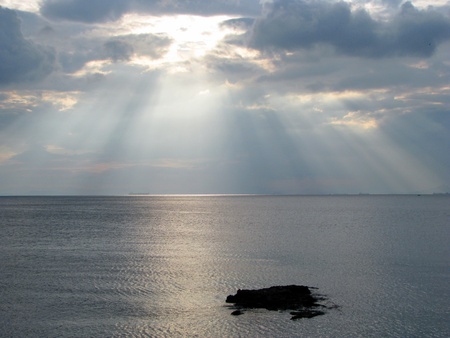 Sun shining through clouds over the seaの写真素材