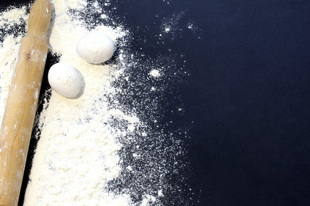 white wheat flour scattered on a black background with a rolling pin