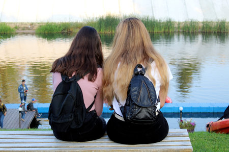 two girls sit with their backs on the riverbank and gossip