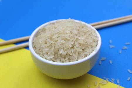 Dry rice lies in a plate and next to it are wooden sticksの写真素材