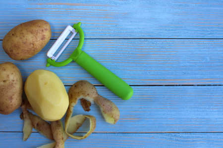 Peeled potatoes with a knife for peeling vegetables on a wooden backgroundの写真素材