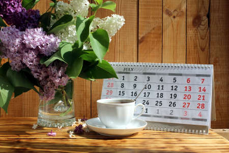 A bouquet of lilacs and a cup of tea on a calendar backgroundの写真素材