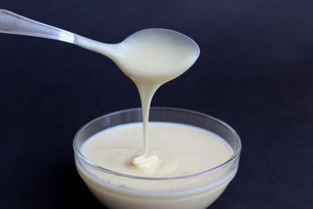 Condensed milk from a boat drains into a glass plateの写真素材