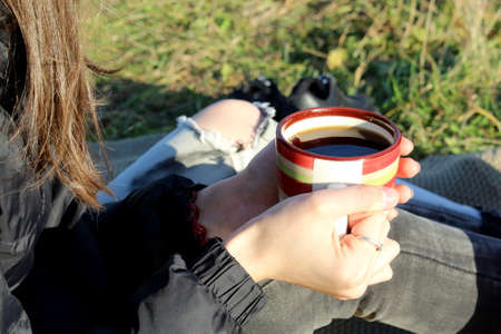 A girl holds a mug of tea in her hands to keep warmの写真素材