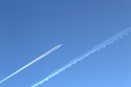 The plane flies high above the ground leaving a white trail. blue blue bright sky without cloudsの写真素材
