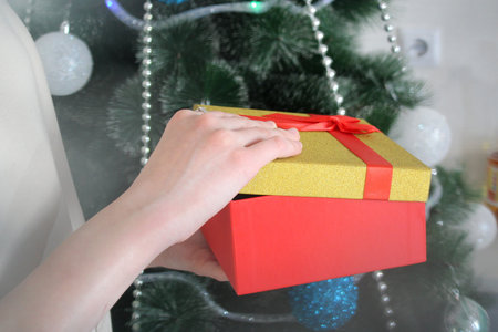 Female hands open a box with a gift on the background of a Christmas tree
