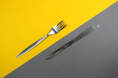 Knife and fork lie on yellow and grayの写真素材