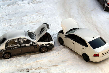 Two cars stand in the winter with open hoods. One car charges anotherの写真素材