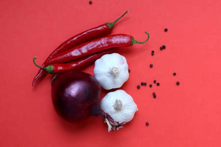 Red pepper, garlic and red onion lie on a red backgroundの写真素材