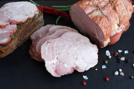 Sliced ham lies on a black stone board with breadの写真素材