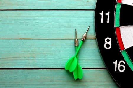 Dart board with two darts lies on a wooden backgroundの写真素材