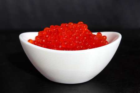 Red caviar in a white small plate on a black backgroundの写真素材