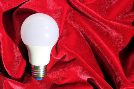 White light bulb lies on red velvet